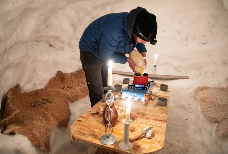 A man sets a table with candles inside an iglu