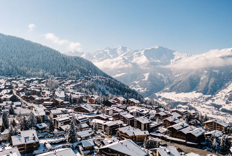 A snowy scene of Verbier village, with snow-covered roofs and big mountains in the distance