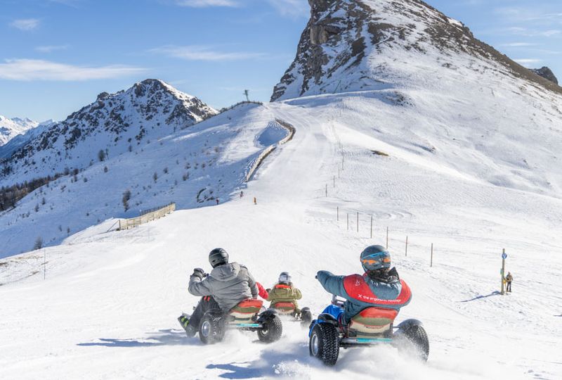 the back of three adults riding mountain karts down an empty ski slope