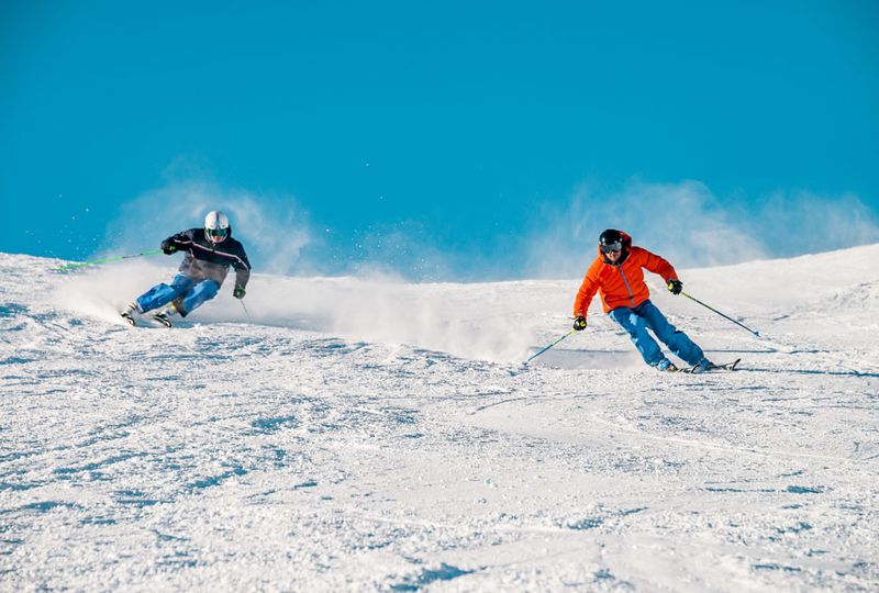 two skiers make turns down a piste, heading straight for camera