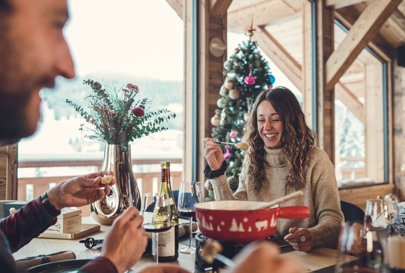 A woman laughs as she eats cheese fondue at an alpine restaurant indoors