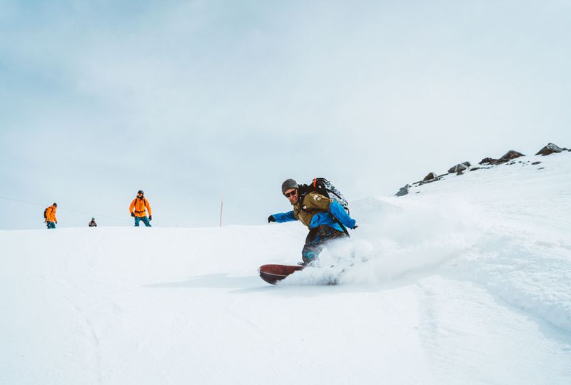 a snowboarder makes a turn spraying powder snow t=downhill towards camera