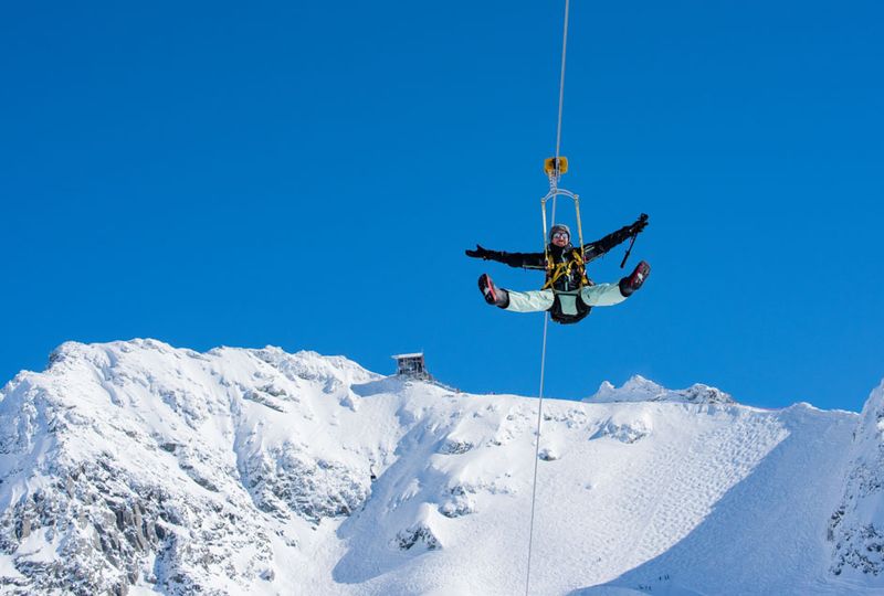 A zipliner flies down the wire with legs and arms out in glee. There's pure blue sky above