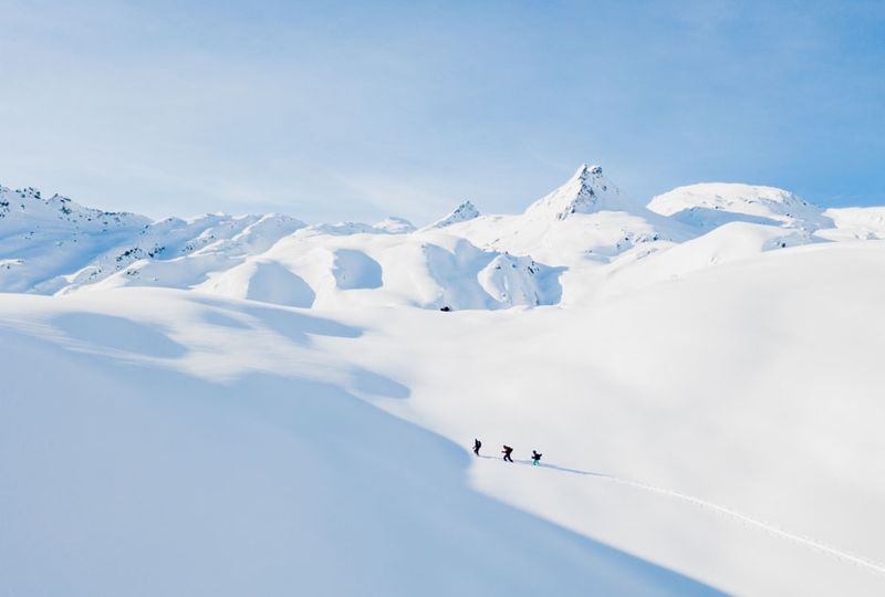 Three ski tourers make their way through a very snowy landscape, near the top of the mountain