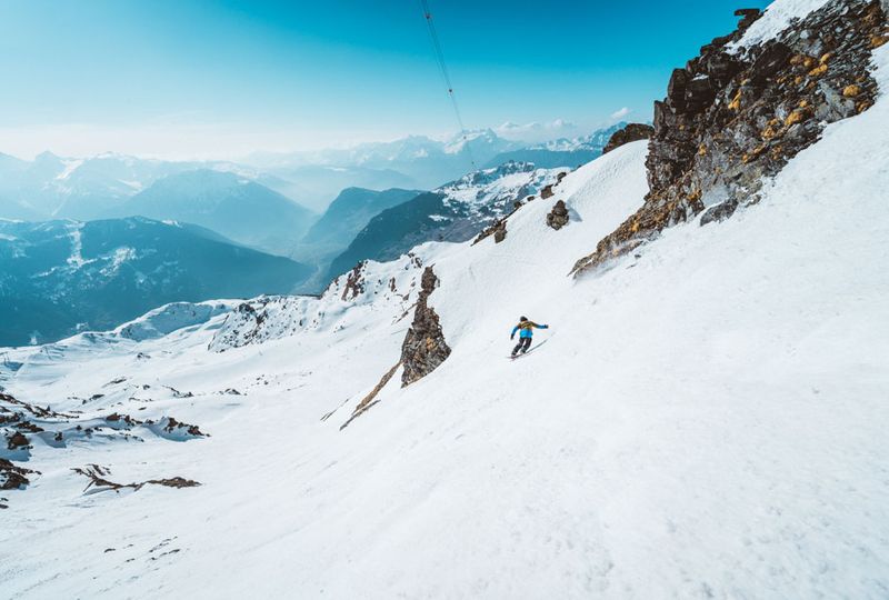 A skier is on a steep, off piste face, beneath rocks