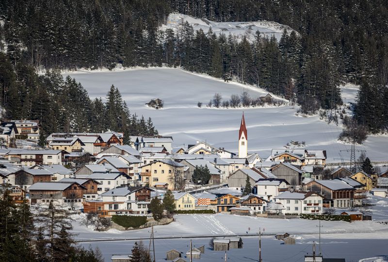 Ski village, surrounded by snowy fields, with the red spire of the village church rising up as the main focus of the picture, taken from afar