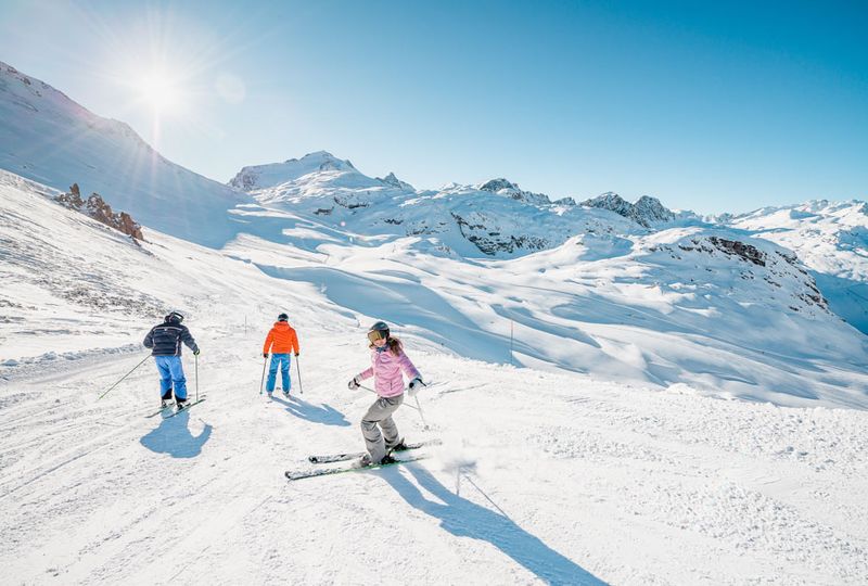 skiers set off down a piste on a blue sky day