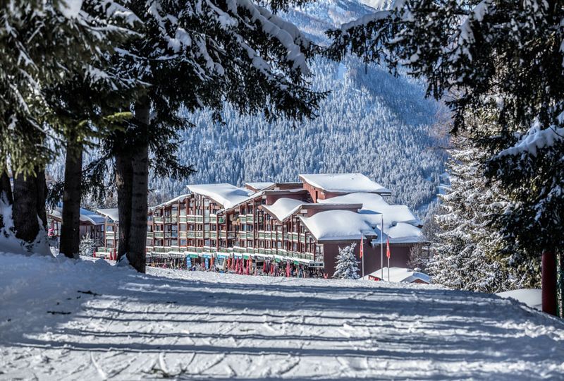 A big snow covered lodge is shot from afar, through a tunnel of trees covered in snow. It's a beautiful image of a snowy mountain building
