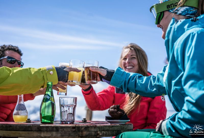 Group of skiers sit outside at a restaurant table cheers-ing beer
