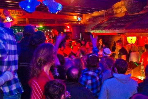 Inside a bar, the lighting is low and red, with a crowd of people under the low ceiling