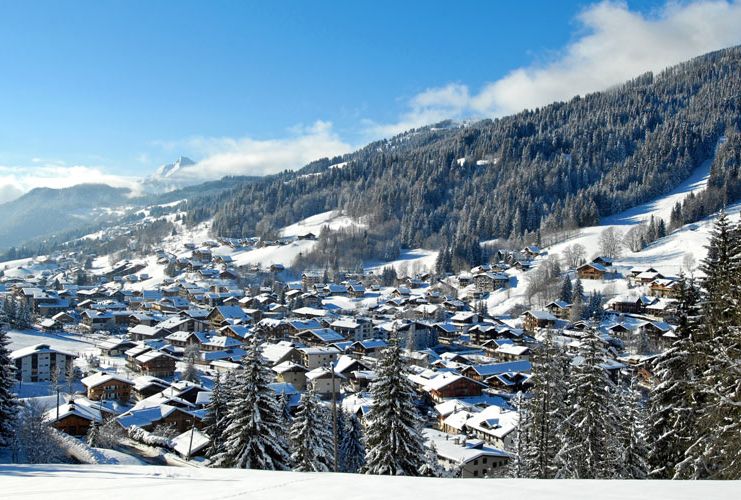 Snowy roofs of a village are shot from on top of a hill, the surroundings covered in snow